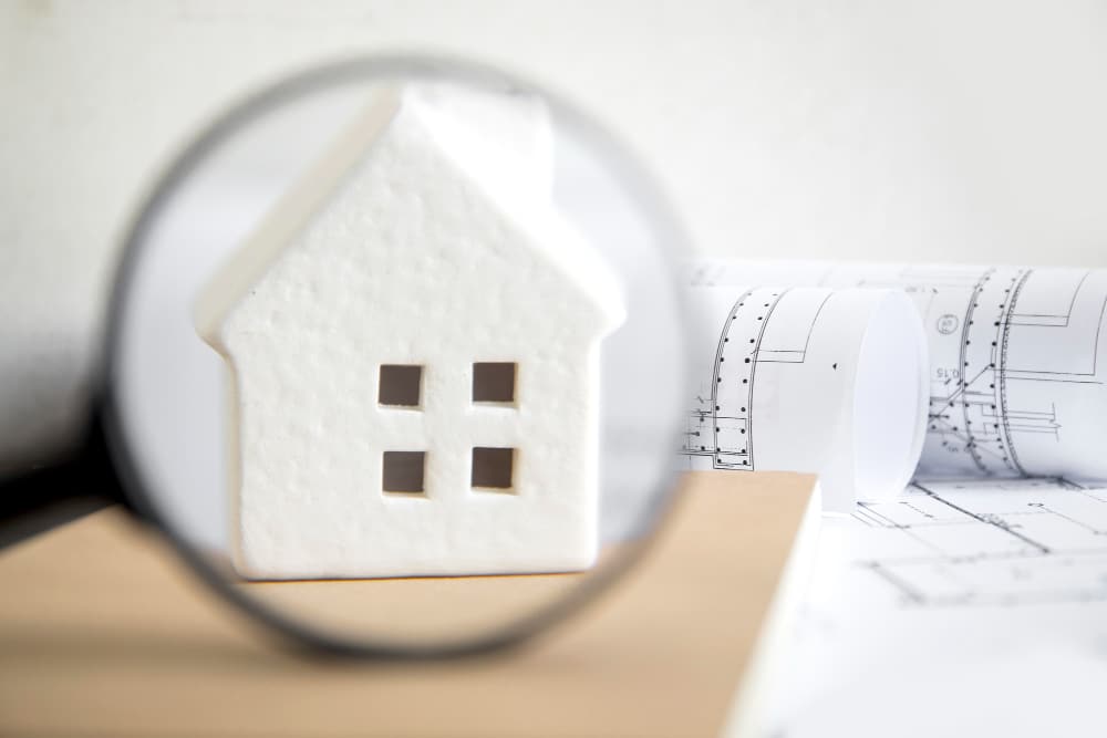 Analyse d’un bien immobilier à la loupe avec plans techniques en arrière-plan